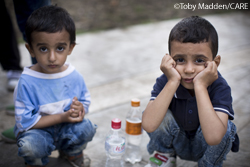 Two young brothers crouching by empty water bottles.