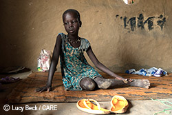 Child from South Sudan sitting on carpet and looking off to the side.