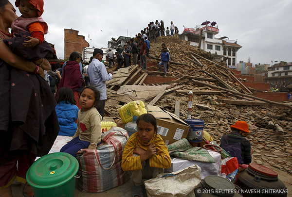 People sit With their belongings outside a damaged temple in
